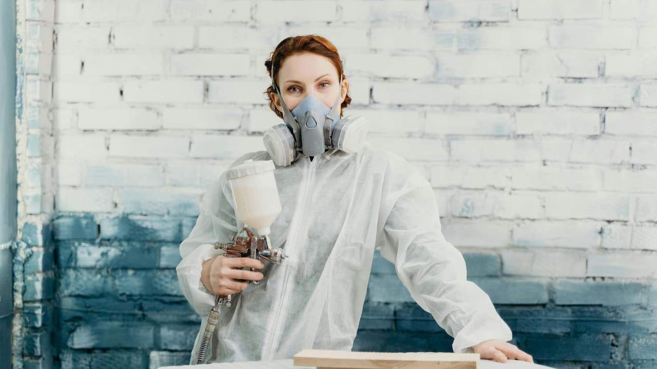 Worker holding a spray paint can, wearing protective gloves, ready to apply paint, outdoor or workshop setting