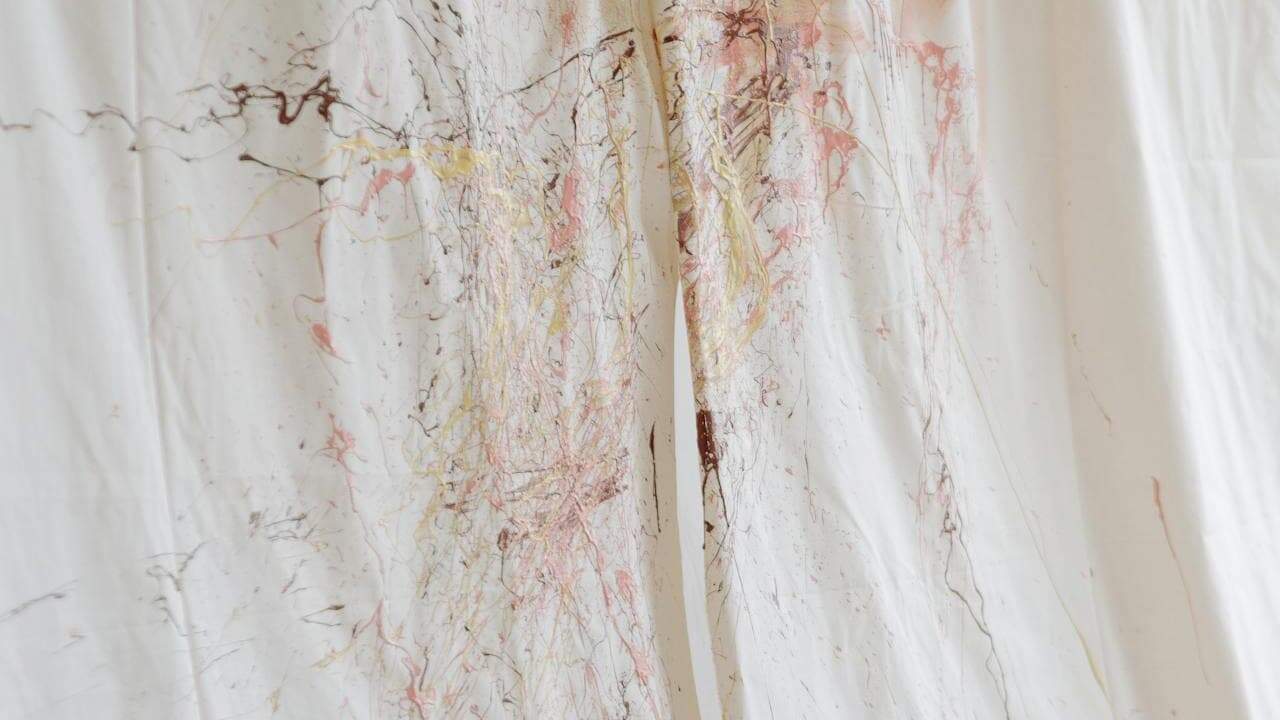 White clothing garments with colorful paint stains and splatters hanging on hangers, showing artistic or work-related marks