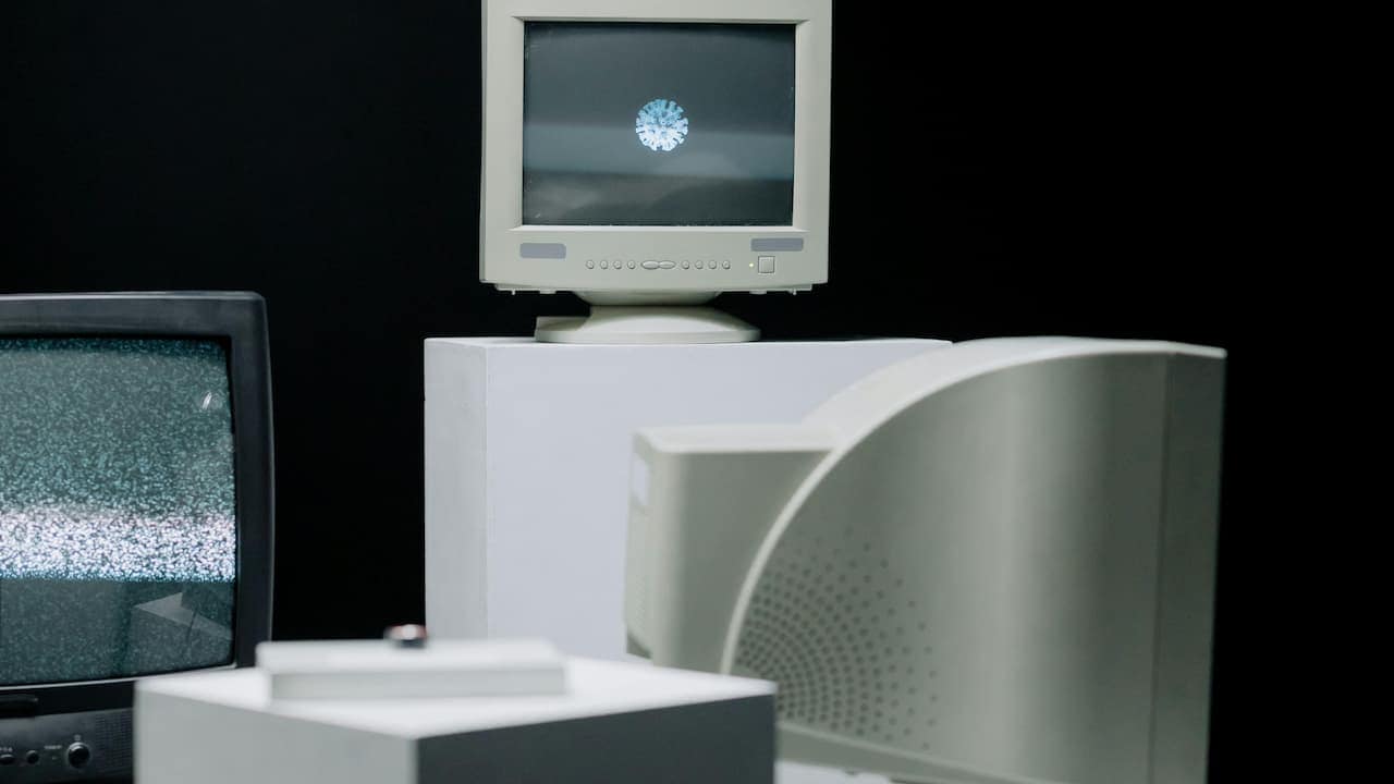 Multiple vintage CRT monitors arranged on white pedestals, one displaying a static screen, another showing a digital virus-like symbol