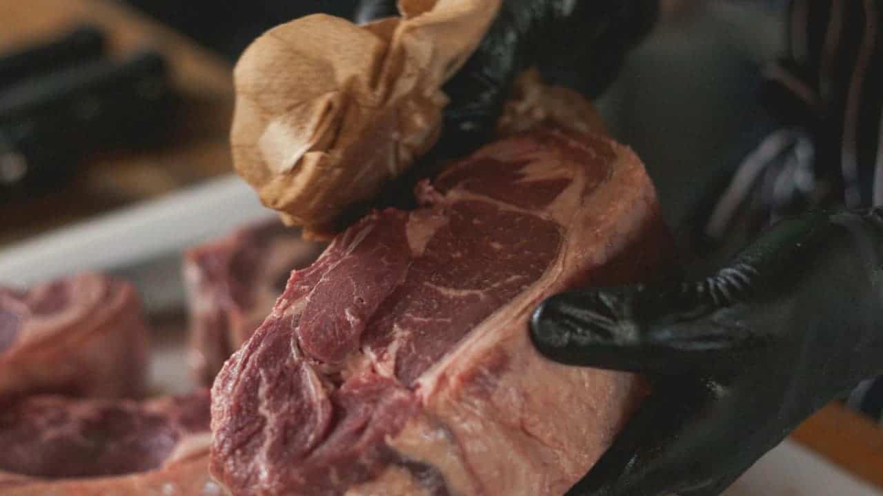 Wet Aged Beef with bone and garlic clove on dark surface, being handled by someone wearing black gloves