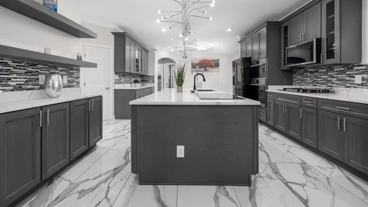 Contemporary kitchen featuring gray cabinetry, white marble flooring, peel-and-stick marble backsplash tiles, central island, and distinctive starburst ceiling light