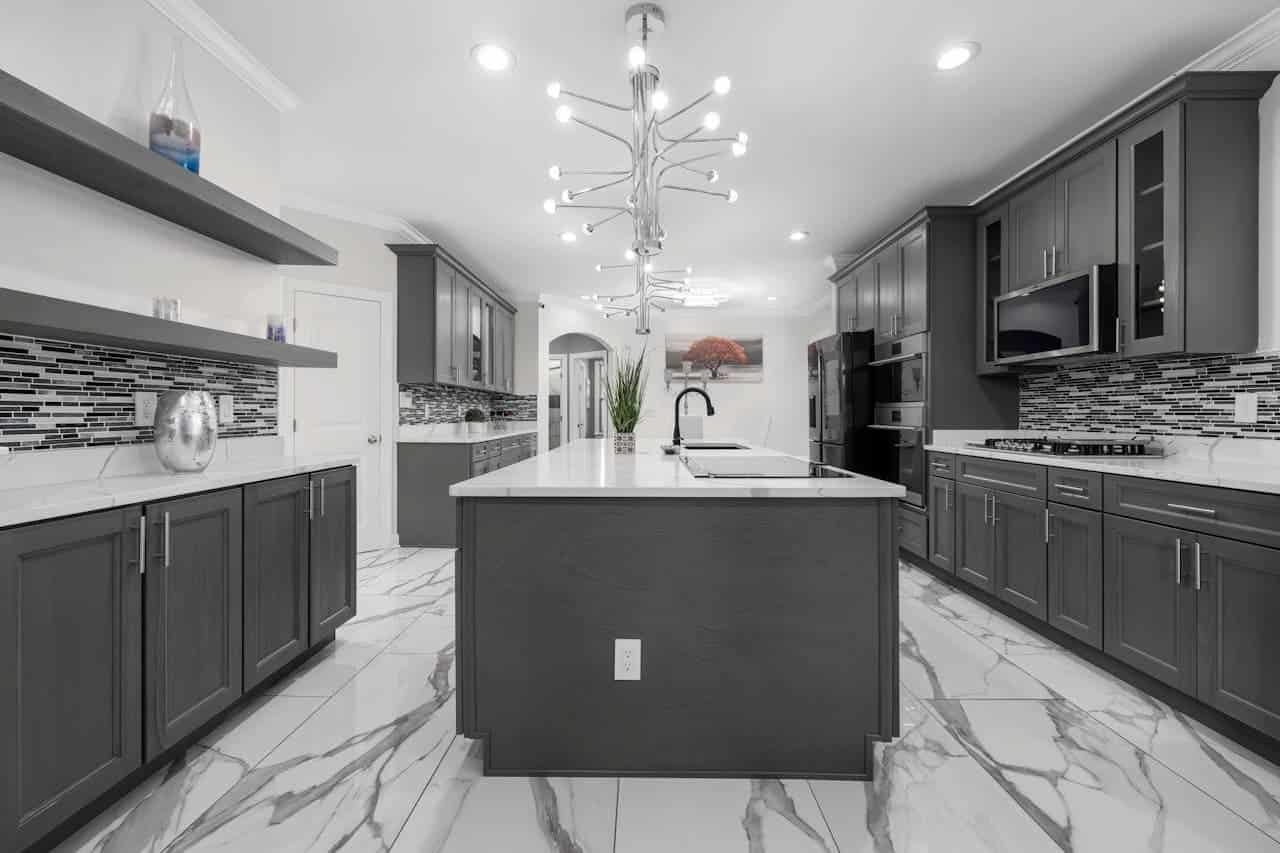 Contemporary kitchen featuring gray cabinetry, white marble flooring, peel-and-stick marble backsplash tiles, central island, and distinctive starburst ceiling light