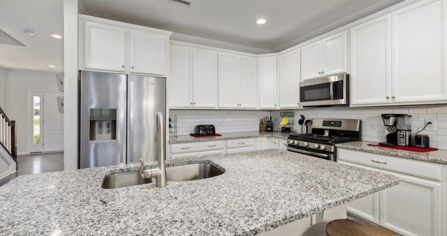 Modern white kitchen with granite countertops, stainless steel appliances, subway tile backsplash, undermount sink, and wooden bar stools