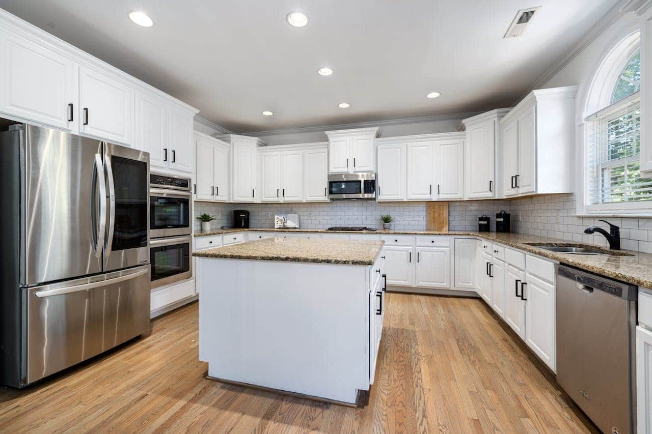 Modern kitchen with white cabinets, granite countertops, stainless steel appliances, hardwood floors, central island, and subway tile backsplash