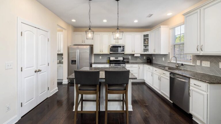 Modern kitchen with white cabinets, dark granite countertops, center island with barstools, stainless appliances, recessed lighting and dark hardwood flooring