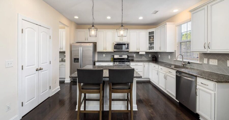Modern kitchen with white cabinets, dark granite countertops, center island with barstools, stainless appliances, recessed lighting and dark hardwood flooring