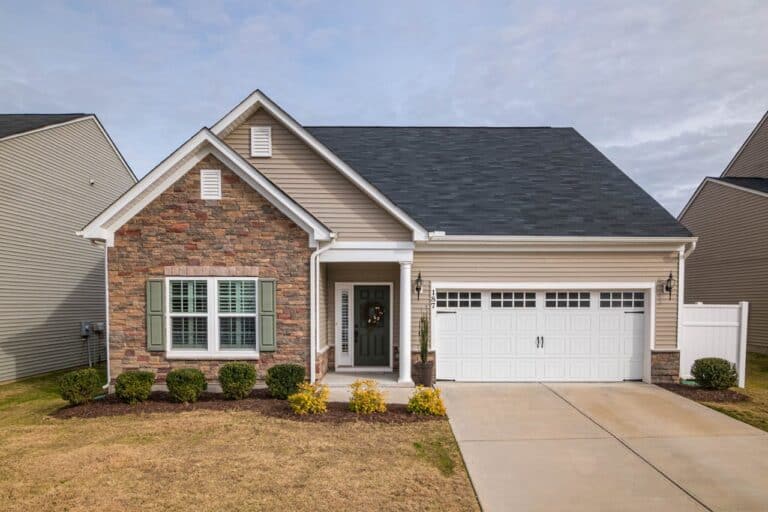 Single-story suburban home with stone and vinyl siding, green shutters, white steel garage door, small front porch, and landscaped yard