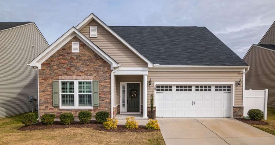 Single-story suburban home with stone and vinyl siding, green shutters, white steel garage door, small front porch, and landscaped yard