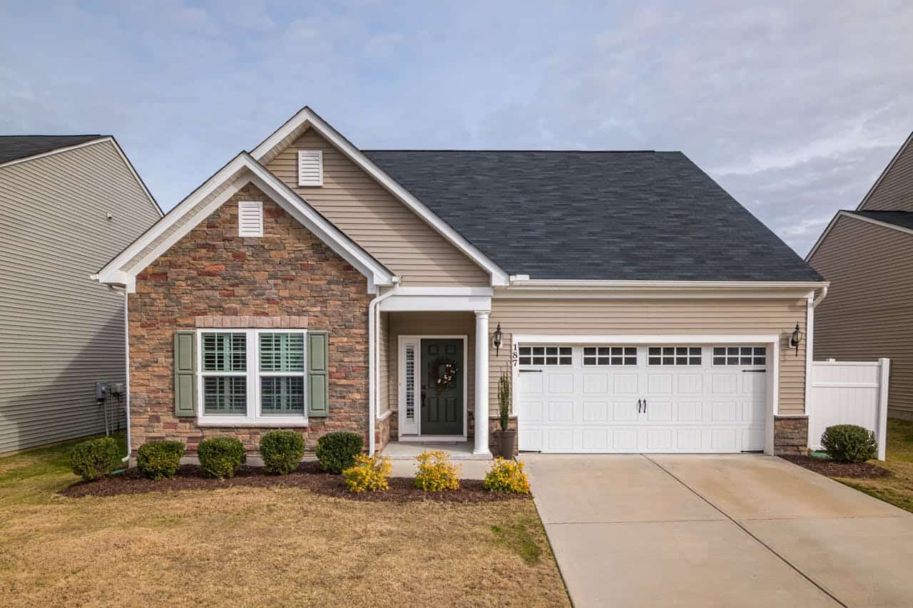 Single-story suburban home with stone and vinyl siding, green shutters, white steel garage door, small front porch, and landscaped yard