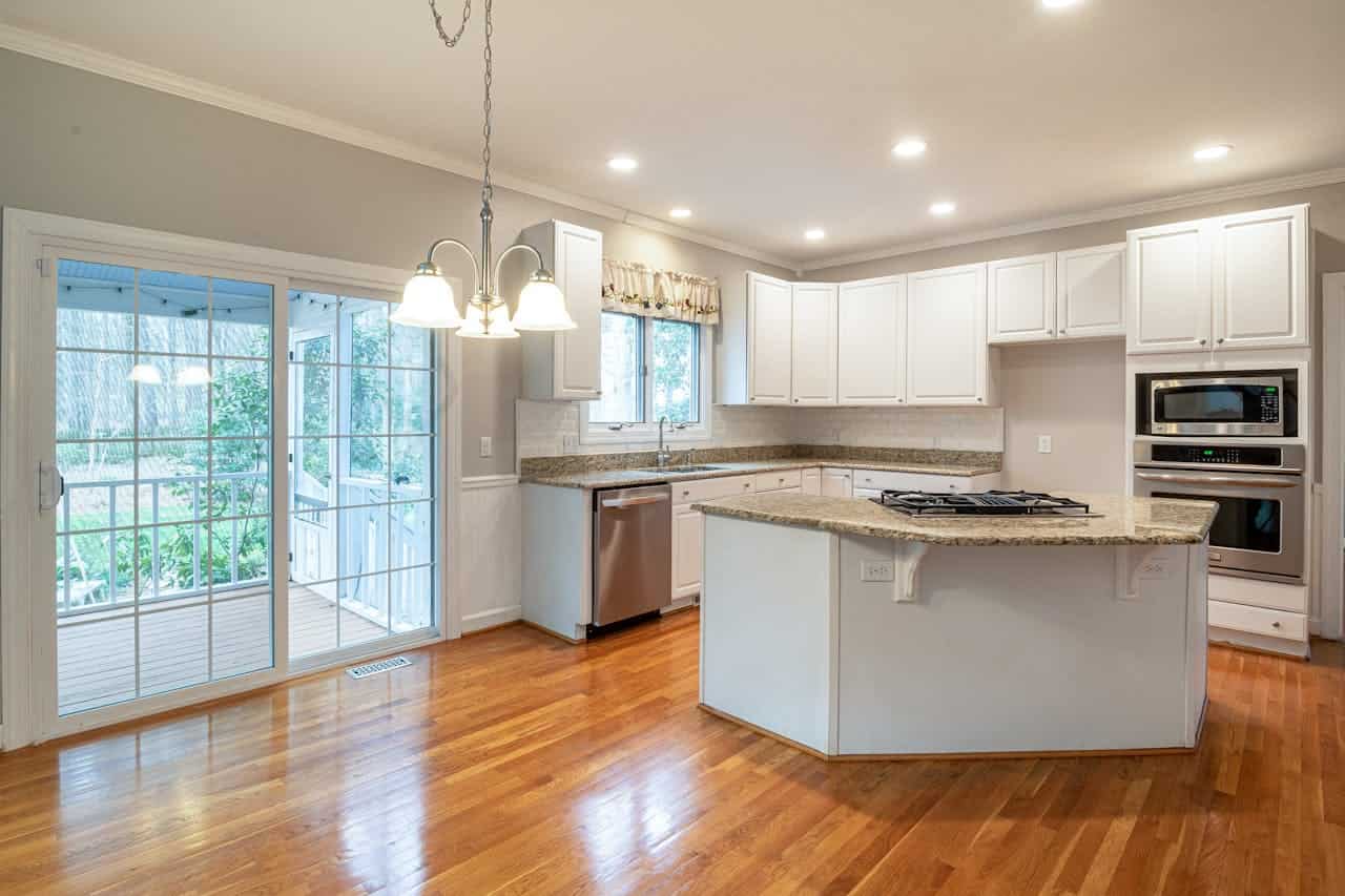 Modern kitchen with white cabinets, granite countertops, stainless appliances, hardwood floors, center island, and sliding glass door to patio