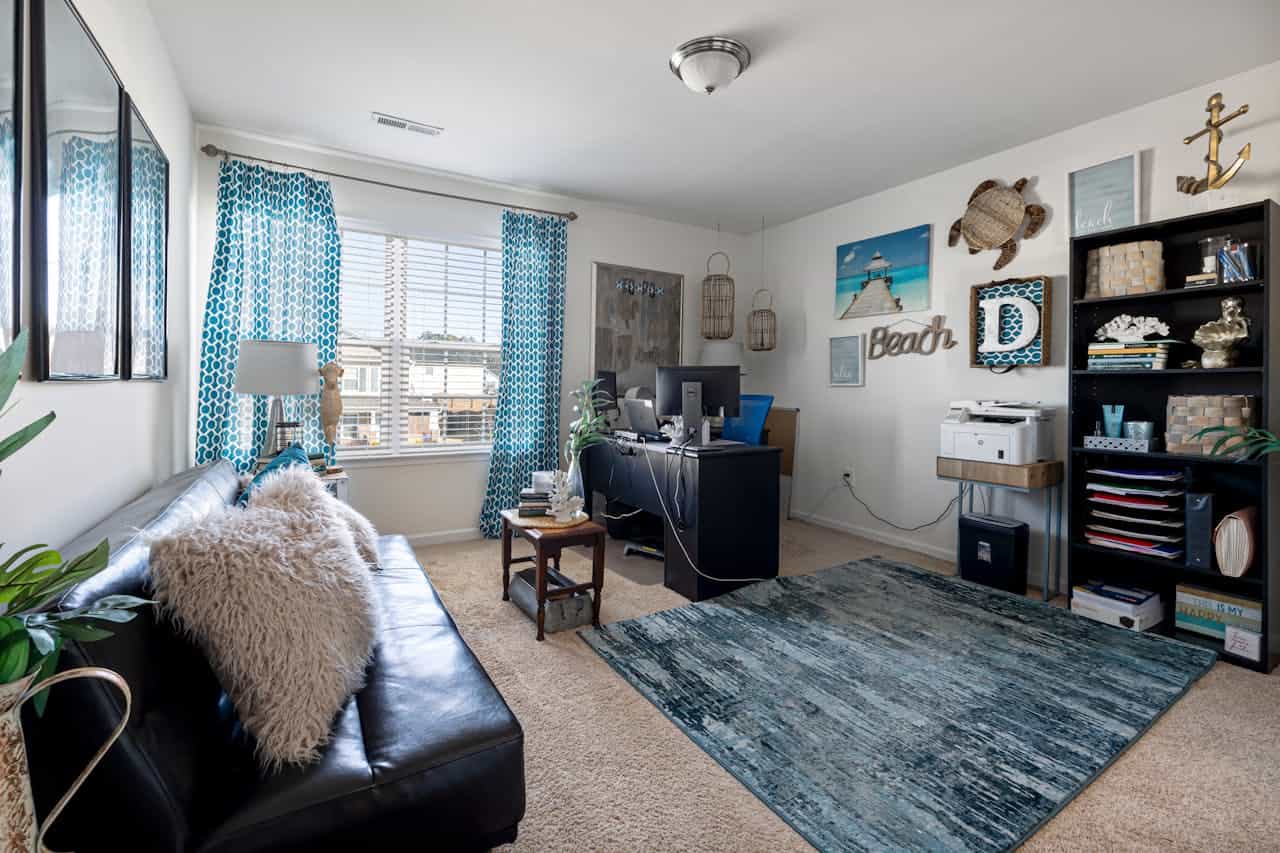 Home office in coastal-themed room with blue curtains, faux fur cushion, black desk, leather sofa, and beach decorations on white walls