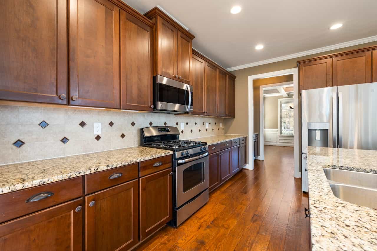 Upscale kitchen with cherry wood cabinets, marble countertops, stainless steel appliances, decorative tile backsplash, and hardwood flooring