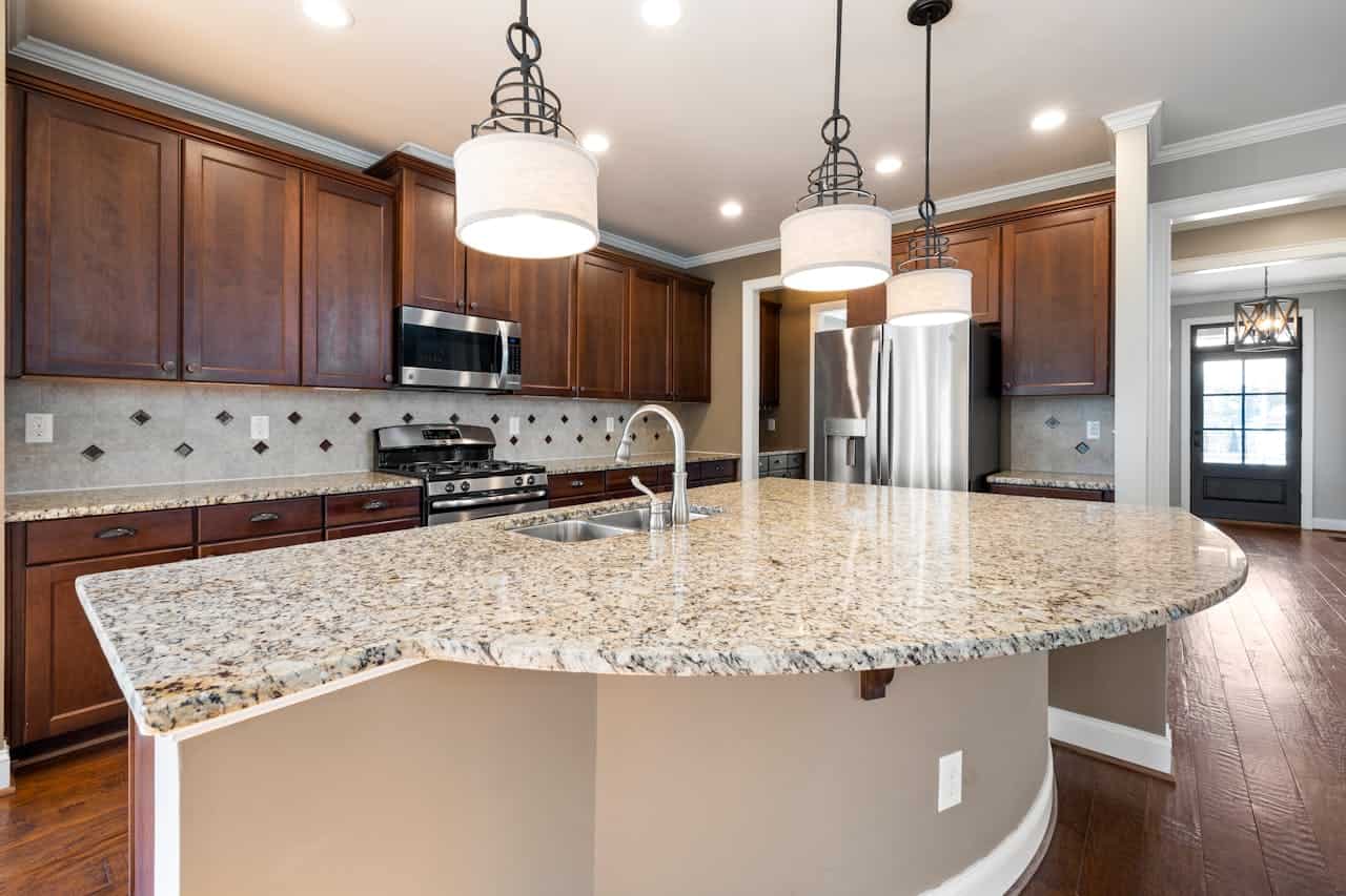 Modern kitchen with curved granite island, dark wood cabinets, stainless appliances, pendant lights, and diamond-patterned backsplash