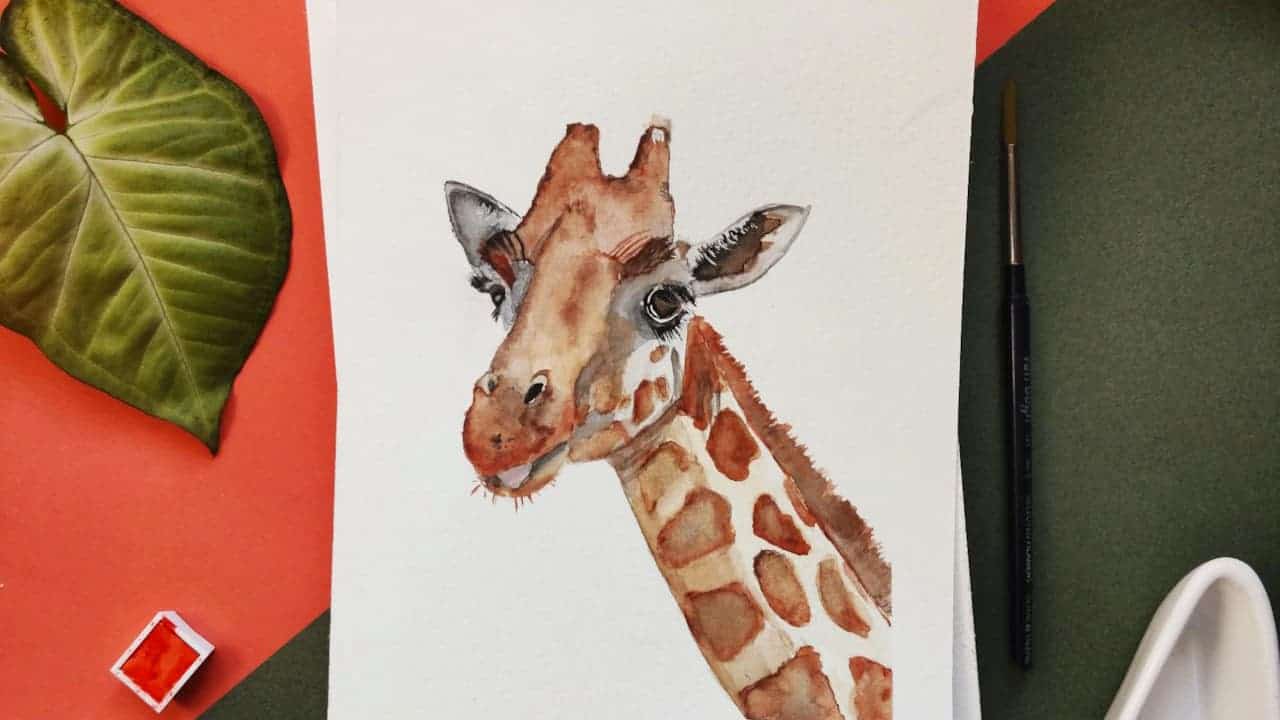 Watercolor painting of giraffe head and neck on white paper, surrounded by art supplies including paintbrush and leaf