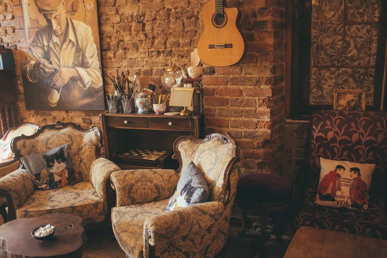 Cozy bohemian living room with quilted upholstery on vintage chairs, exposed brick wall, acoustic guitar, art supplies, and decorative pillows