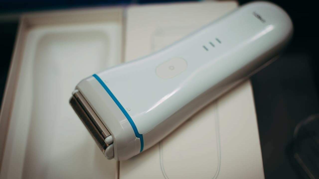 White Braun electric razor with blue accent trim resting on white packaging box against dark blurred background