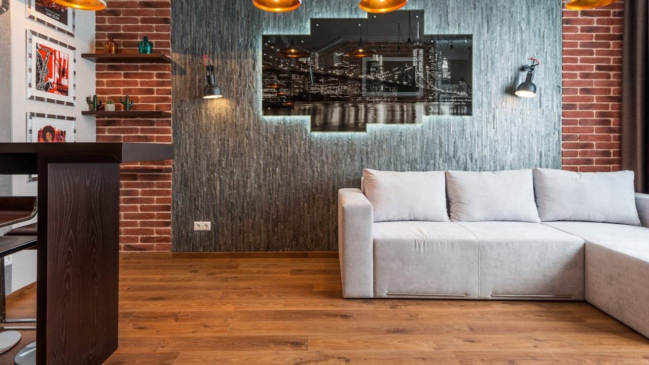 Modern industrial living room with white sectional sofa, exposed brick walls, pendant lights, and NYC skyline artwork on textured wall