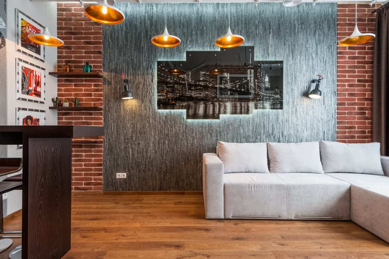 Modern industrial living room with white sectional sofa, exposed brick walls, pendant lights, and NYC skyline artwork on textured wall