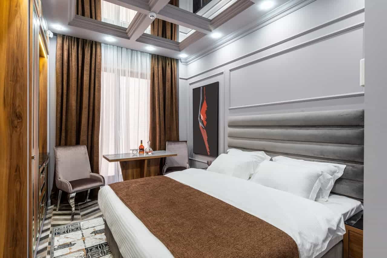 Luxurious bedroom with white bed, brown runner, gray padded headboard, mirrored ceiling, wooden wardrobe, and small dining table