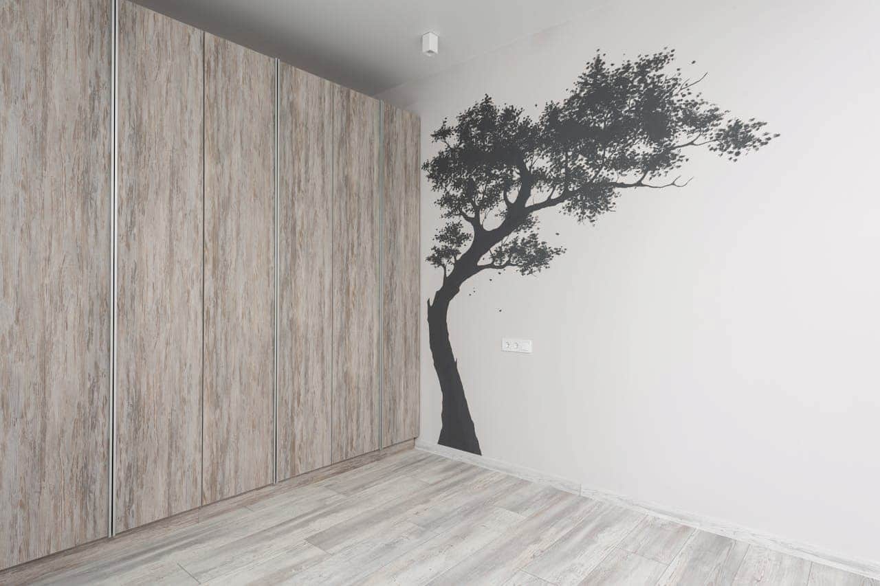 Minimalist room with light wood floors and closets, featuring a black tree silhouette painted on white wall
