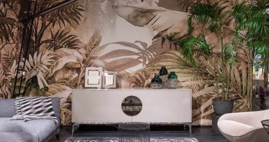 Modern living room with tropical palm wallpaper, white credenza, gray sofa, wire coffee table, cream chair, and potted plants