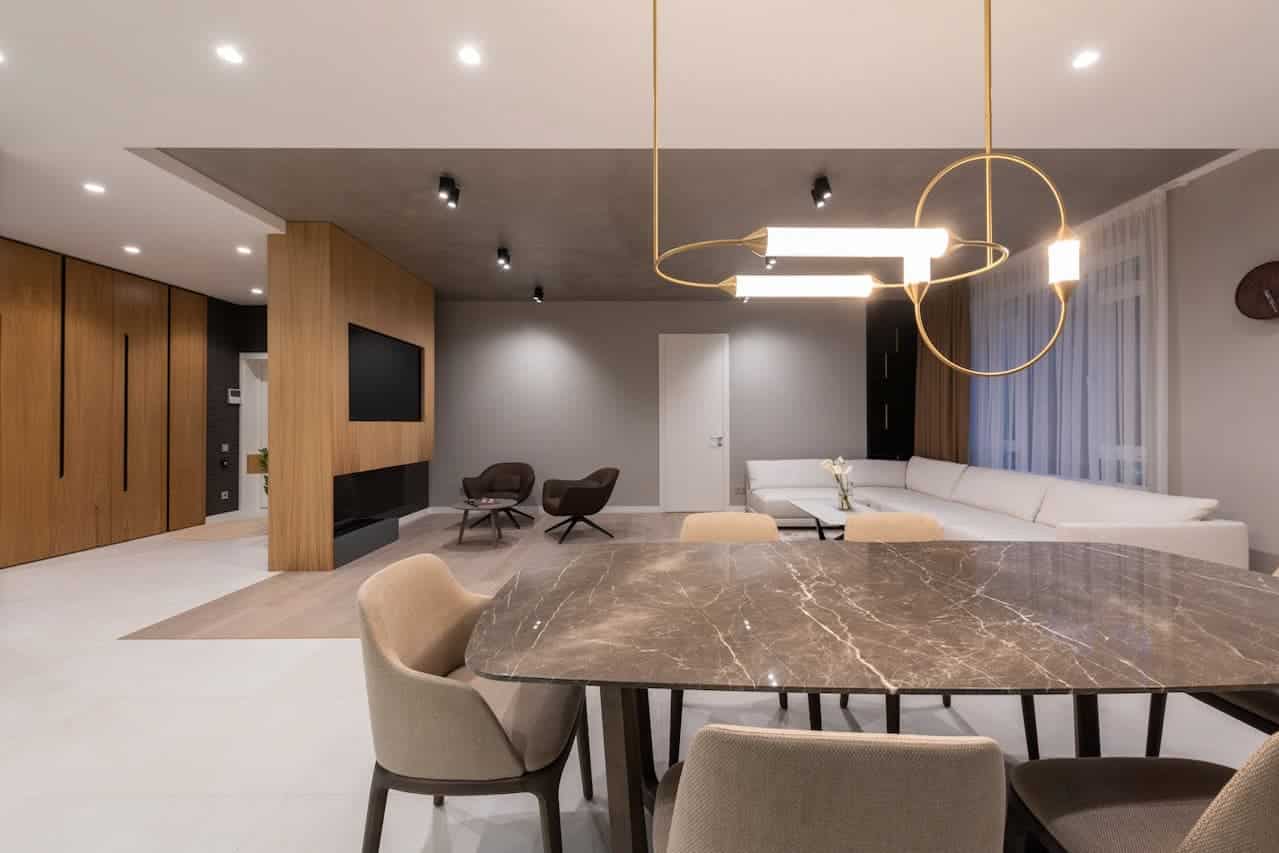 Modern open-concept living space with marble dining table, geometric pendant light, white sectional sofa, wood paneling, and minimalist decor