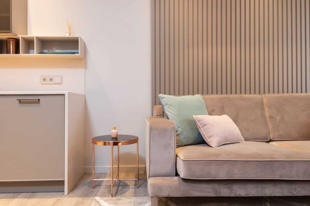 Modern living room with beige sofa, teal and pink pillows, gold side table, and white storage cabinet against striped wall