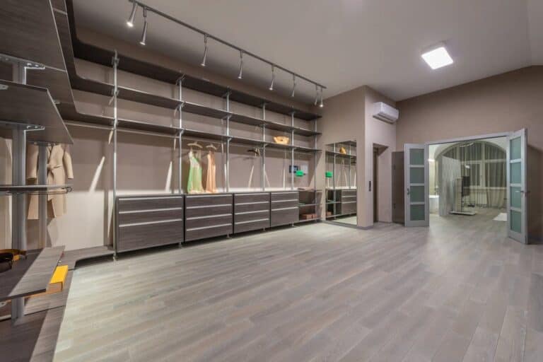 Spacious walk-in closet with gray wood flooring, track lighting, built-in shelving, drawers, and hanging sections for formal dresses