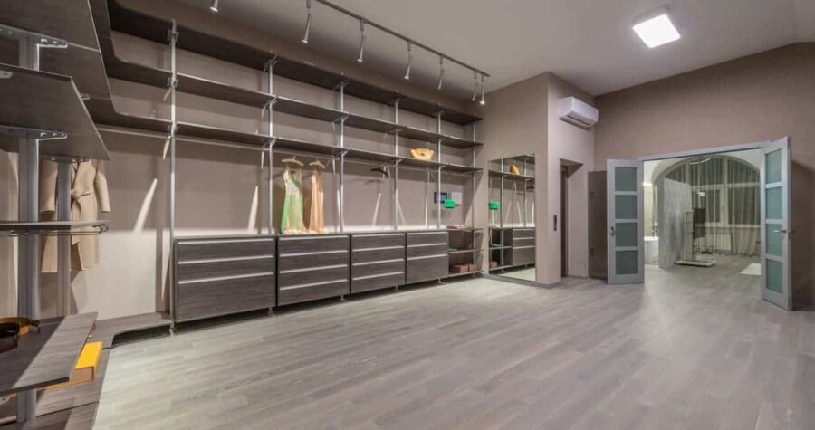 Spacious walk-in closet with gray wood flooring, track lighting, built-in shelving, drawers, and hanging sections for formal dresses