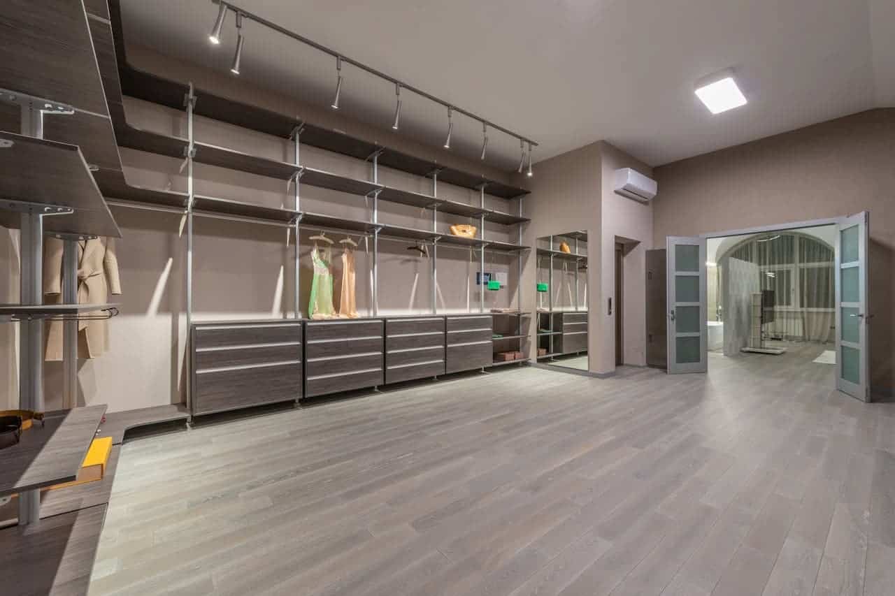 Spacious walk-in closet with gray wood flooring, track lighting, built-in shelving, drawers, and hanging sections for formal dresses