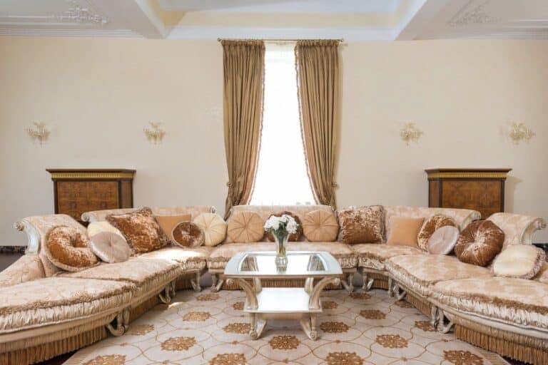Luxurious cream-colored sectional sofa with decorative pillows in elegant living room featuring glass coffee table and beige curtains