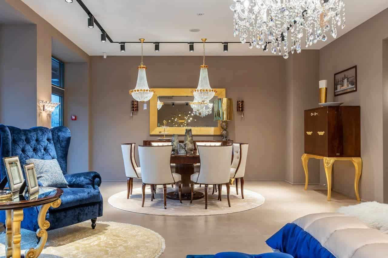 Luxurious dining room with crystal chandeliers, round table with white chairs, blue velvet armchair, and gold accents