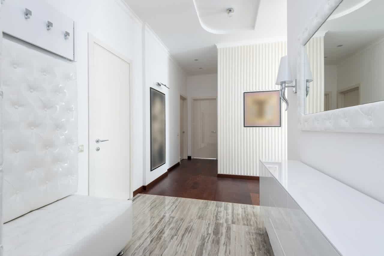 Modern white hallway with quilted wall panels, marble-look flooring, dark wood floors, striped wallpaper, wall sconces, and multiple doorways