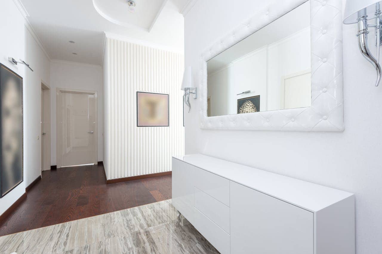 Modern hallway with white walls, textured accent wall, wood flooring, white console table, framed mirror, and minimalist decor