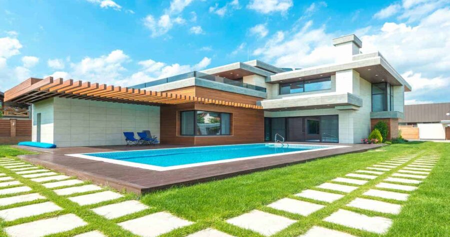 A modern luxury home with a geometric design, featuring a pristine synthetic garden pool bordered by wooden decking