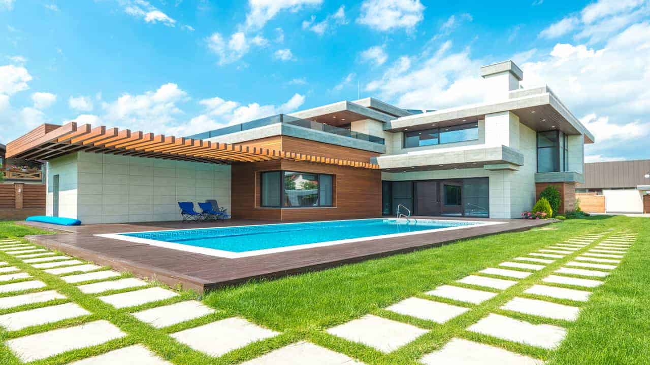 A modern luxury home with a geometric design, featuring a pristine synthetic garden pool bordered by wooden decking