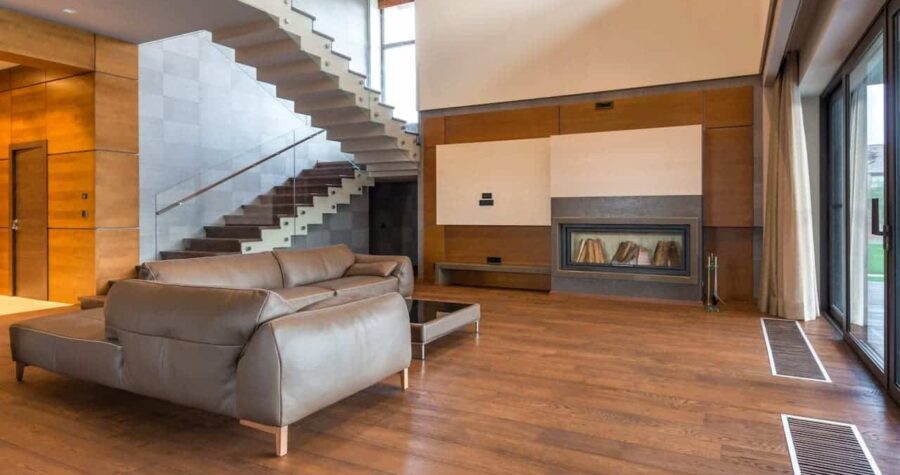 Modern living room with Stark minimalism, floating staircase, gray leather sectional sofa, built-in fireplace, wood paneling, and large windows with natural light