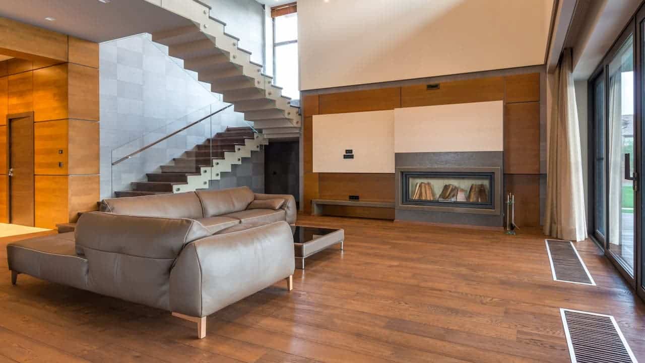 Modern living room with Stark minimalism, floating staircase, gray leather sectional sofa, built-in fireplace, wood paneling, and large windows with natural light