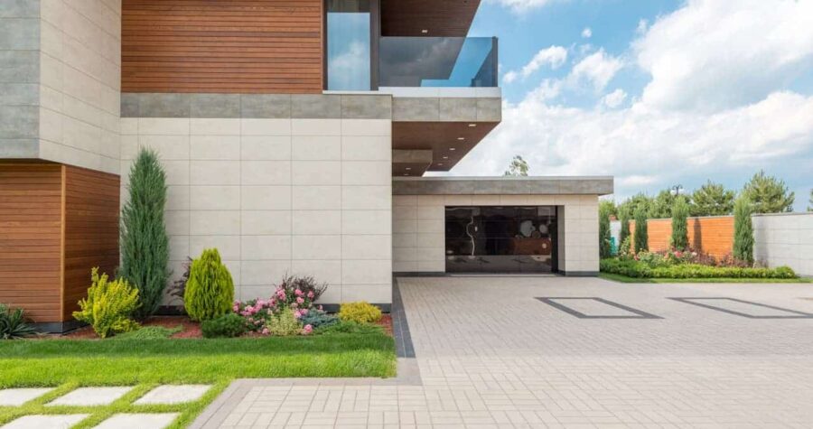 Modern house with clean lines, beige and wood-paneled walls, manicured garden, glass balcony, concrete paver edging, and blue sky backdrop