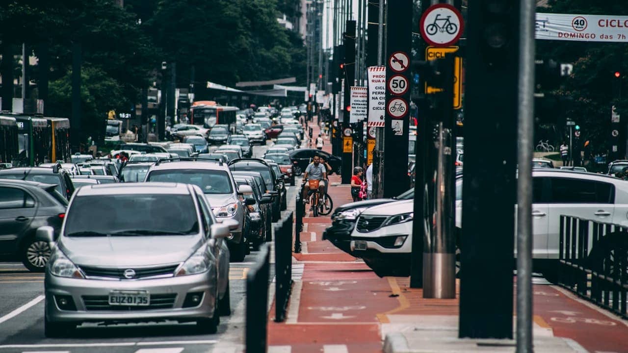 Heavy traffic congestion on urban street with dedicated red bike lane, multiple cars, buses, traffic signs, and cyclists navigating city infrastructure