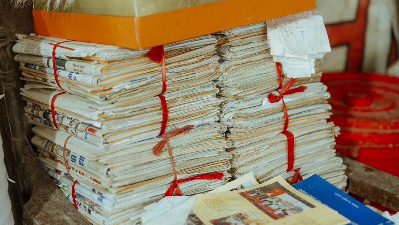 Stacks of old newspapers and documents tied with red string, with yellowing pages and an orange box above