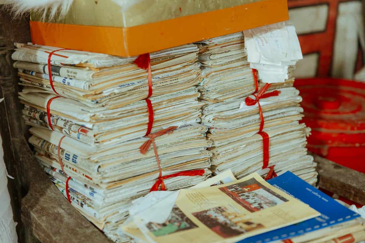 Stacks of old newspapers and documents tied with red string, with yellowing pages and an orange box above
