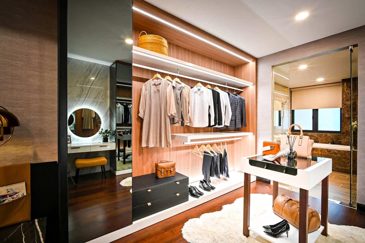 Luxurious walk-in closet with wood paneling, hanging clothes, display island, leather accessories, mirror, and glimpse of adjoining bathroom