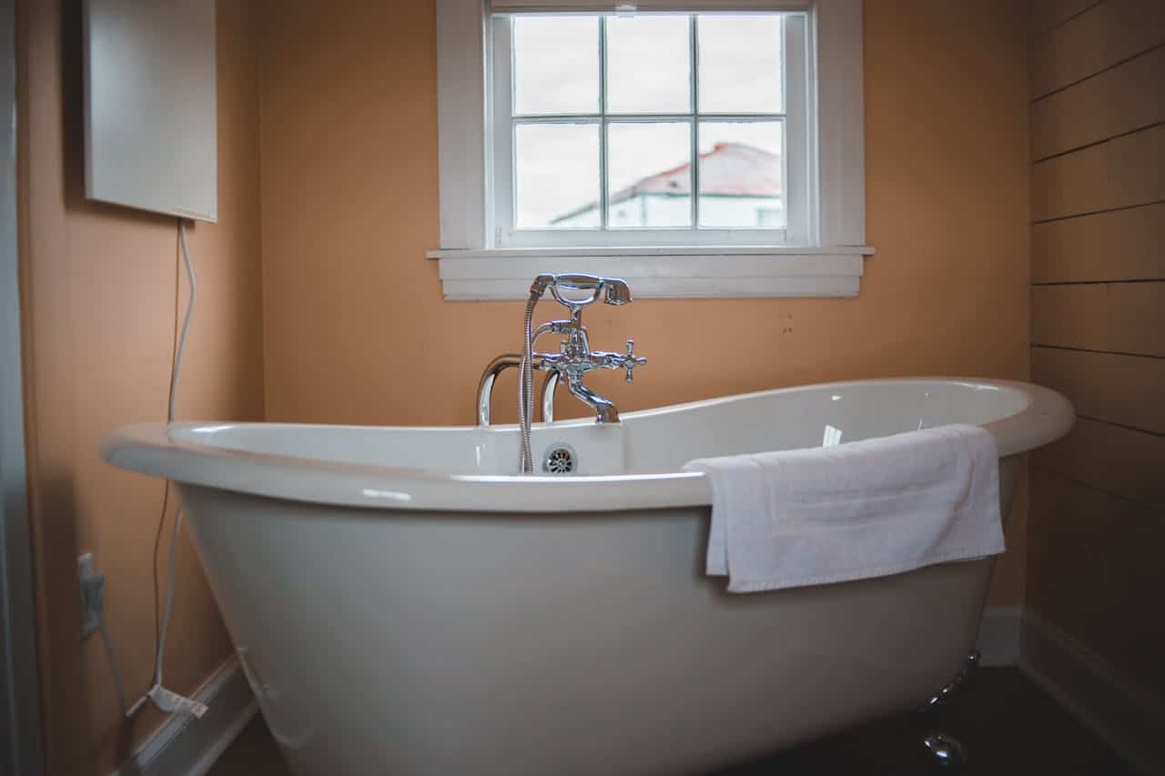 White clawfoot bathtub with chrome fixtures in a bathroom with peach walls, wooden paneling, and window
