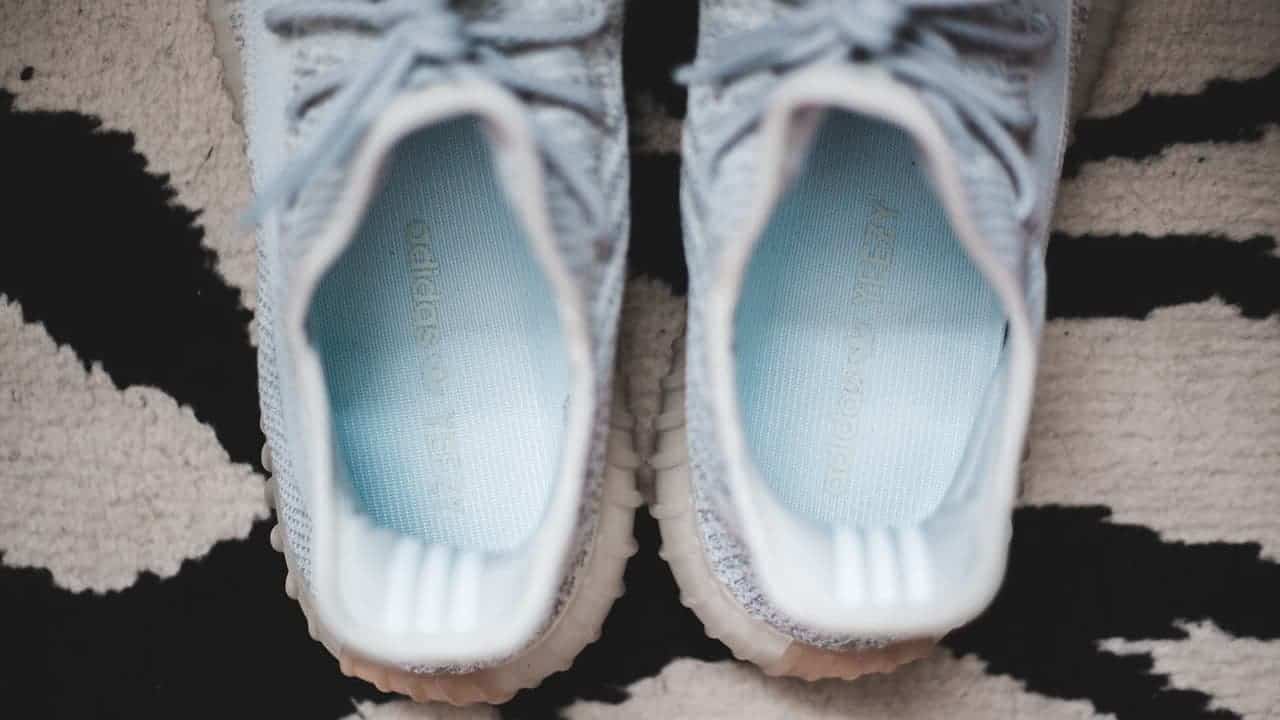 Pair of white Adidas sneakers with light blue insoles placed on black and white striped rug