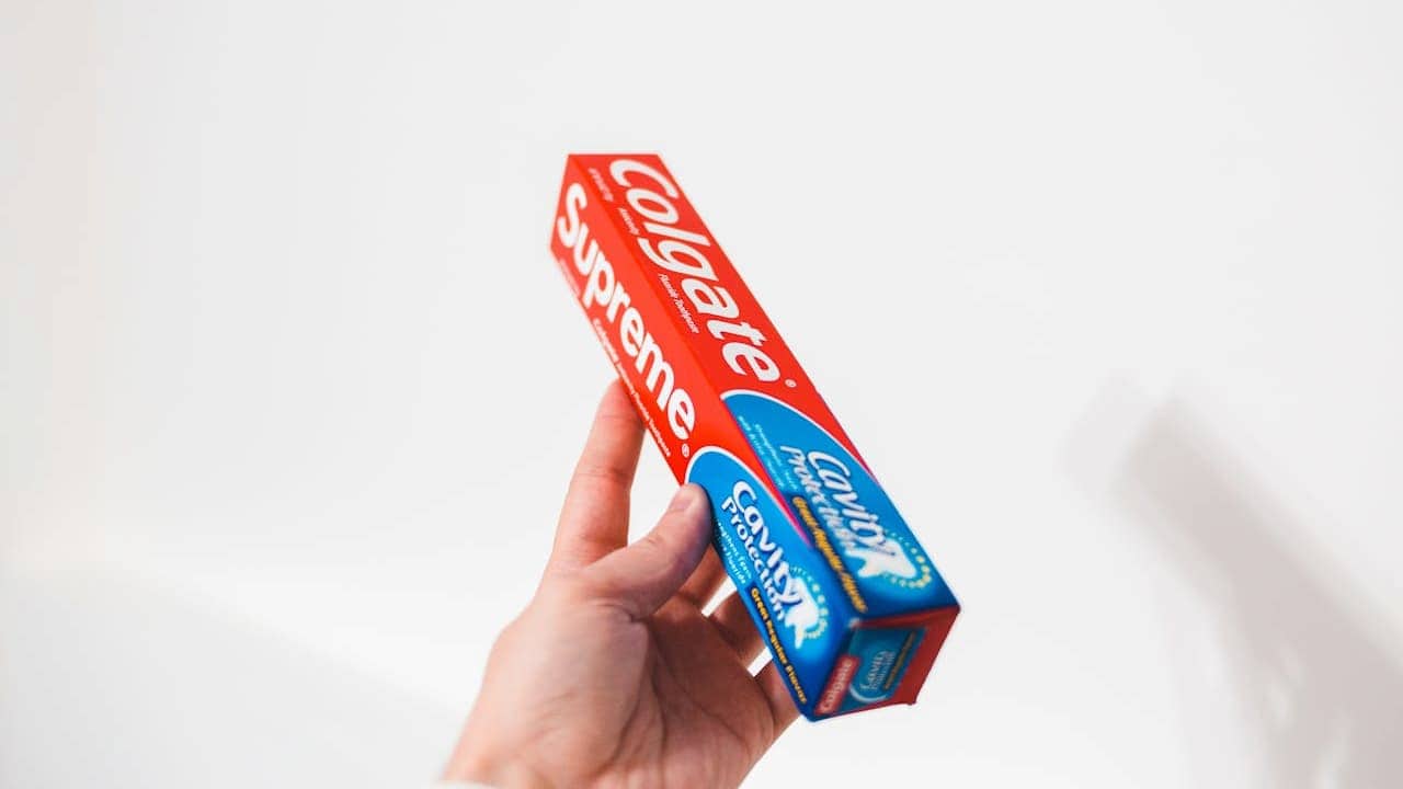 Hand holding Colgate Supreme toothpaste box with red and blue packaging against white background in product display