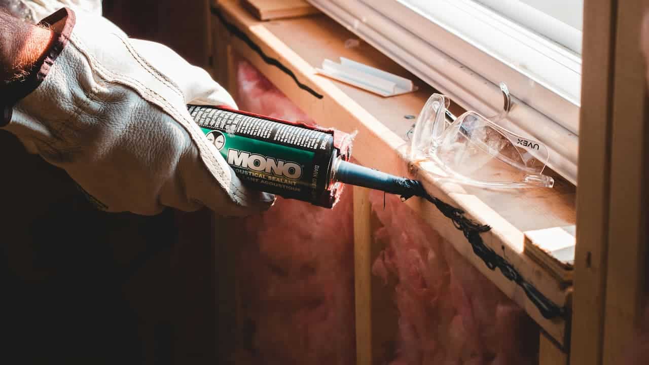 Worker applying Gorilla Heavy Duty Construction Adhesive from a tube with a nozzle, wearing gloves, focusing on bonding surfaces