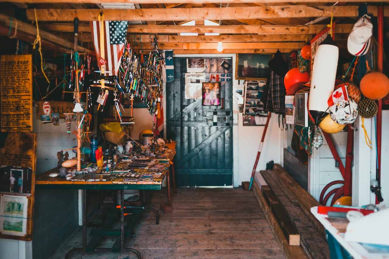Rustic wooden workshop or cabin interior with American flag, fishing buoys, cluttered workbench, and nautical memorabilia around doorway