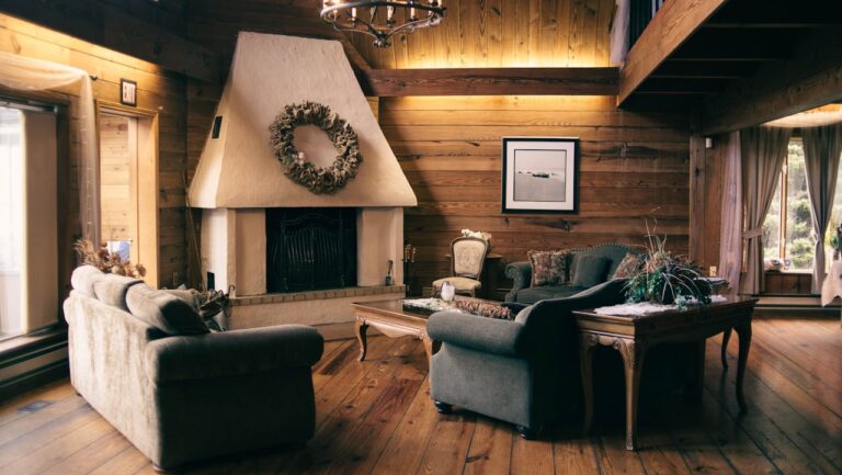 Cozy rustic cabin living room with wooden walls, white fireplace, chandelier, comfortable sofas, and natural light