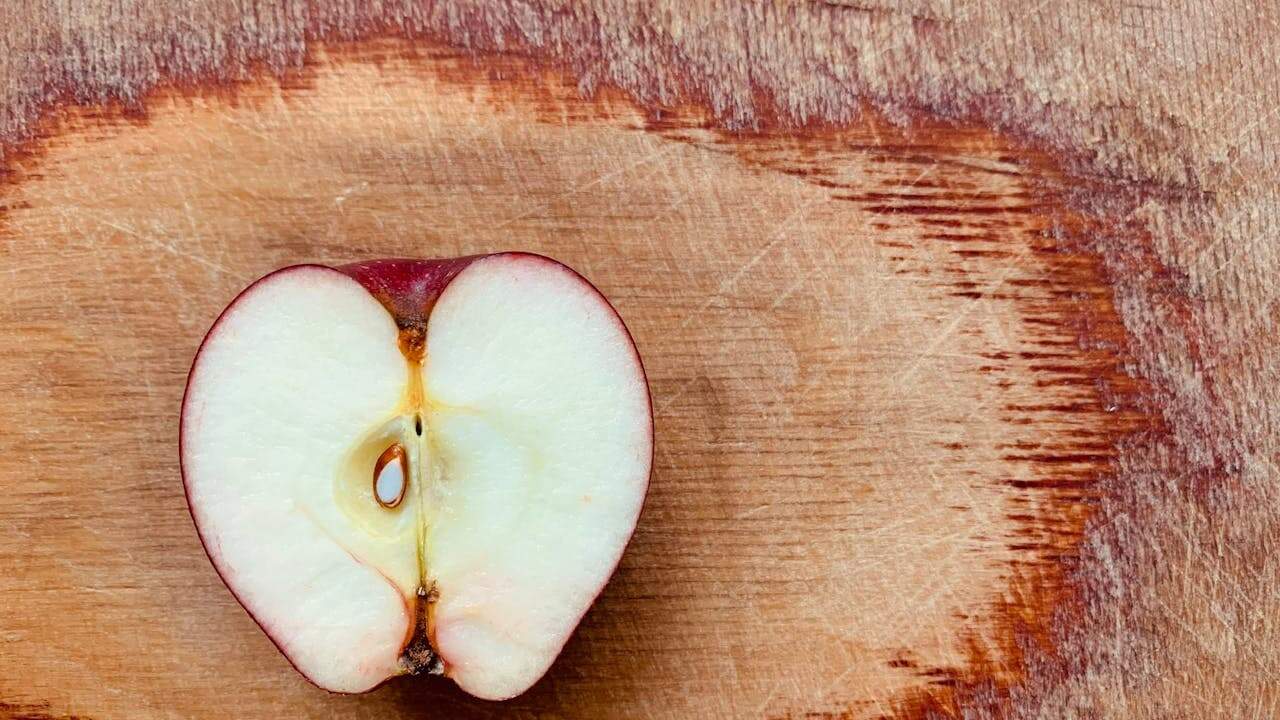 Half of a red apple cut crosswise on a wooden cutting board, showing white flesh and brown seed